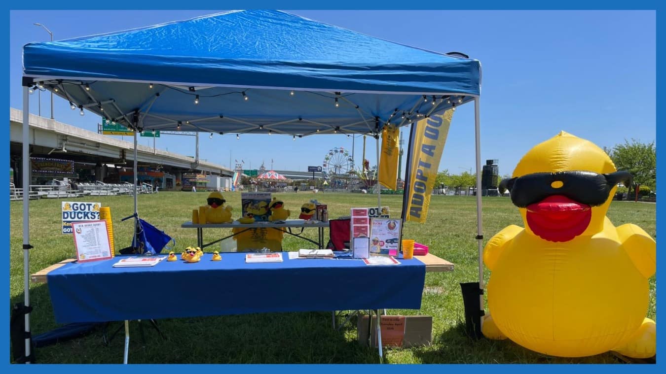 The duck adoption booth under a blue tent beside a giant inflatable duck