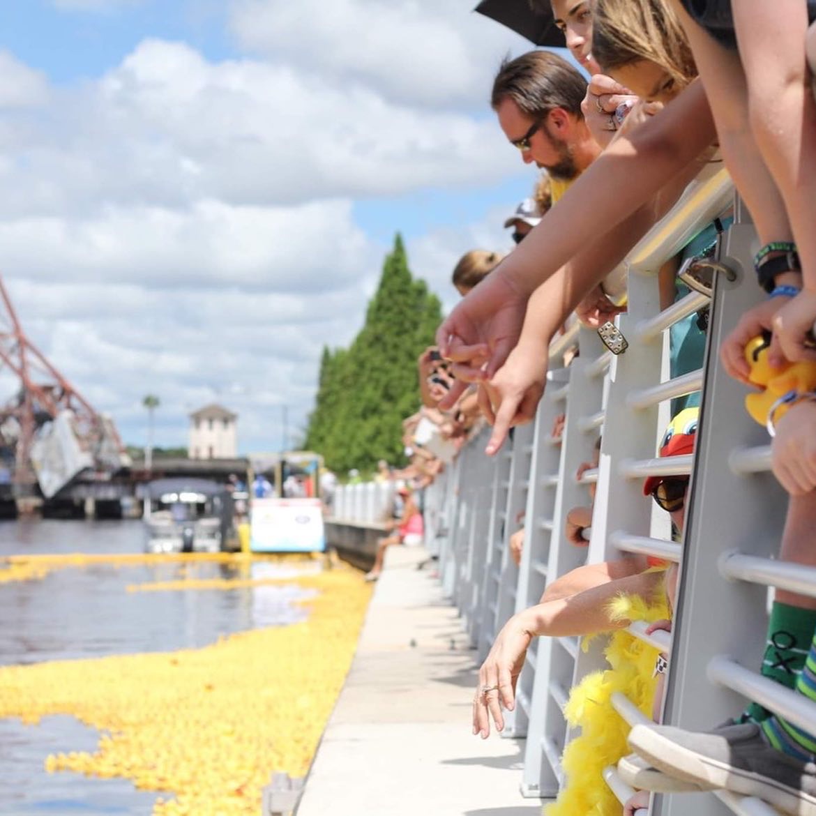 Neighbors leaning over the railing as a raft of yellow ducks floats past below